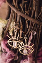 Load image into Gallery viewer, Brass gold toned earring in an eye shape with a crystal quartz in the center hanging from a wooden wreath.